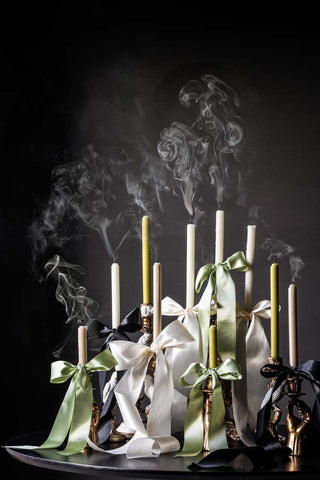Lifestyle image of several dinner candles at different heights which have just been extinguished, decorated with ribbons. 