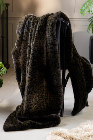 The Jaguar Faux Fur Throw shown draped over a black chair in a room with neutral panelled walls. 