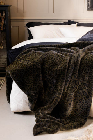 The Jaguar Faux Fur Throw shown on a bed with black and white bedding. 