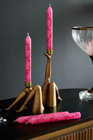 Lifestyle image of two different leg candle holders displayed on a black sideboard with pink patterned candles and a table lamp.