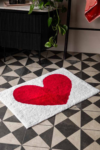 The LOVE Tufted Cotton Bath Mat style on a geometric patterned floor, in front of a black cupboard and towel rack, soap dispensers on a tray, plant and a towel.