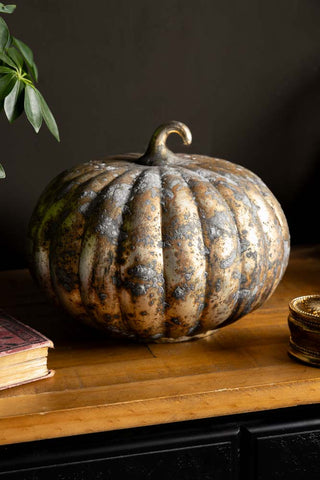 Image of a Large Rustic Patina Glass Pumpkin shown on a wooden sideboard with a dark wall. 