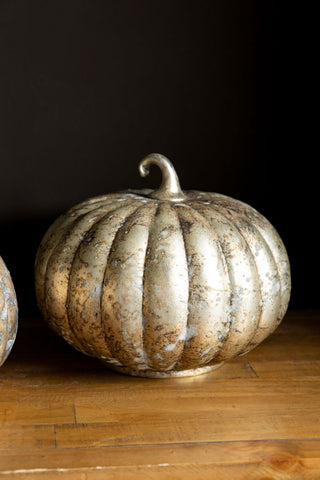 The Large Rustic Patina Glass Pumpkin shown against a dark wall on a wooden surface. 