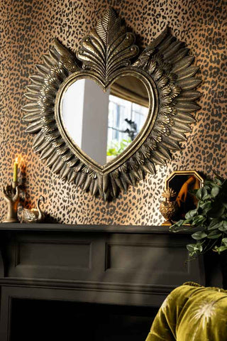 The Large Winged Milagro Mirror on a leopard print wall above a fireplace with various accessories on the shelf beneath.