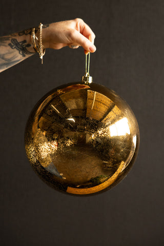 The Large Antique-Style Gold Christmas Bauble being held up in front of a dark wall.