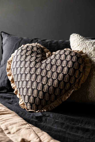 Beautiful fern leaf heart-shape cushion styled on a bed with charcoal linen bed sheets.