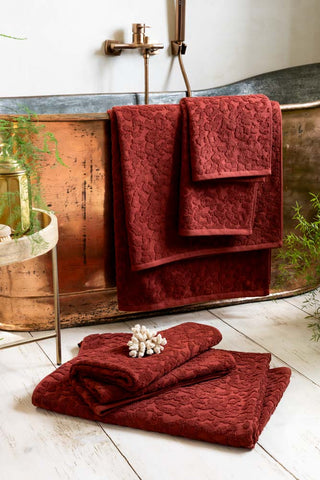 all the sizes of the Leopard Jacquard Towels in Burnt Brick shown together in a bathroom with a copper bath and white wood floors. 