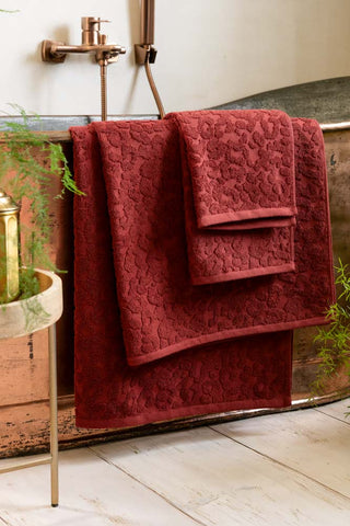 Three of the Leopard Jacquard Towels in Burnt Brick folded over the top of a copper bath. 