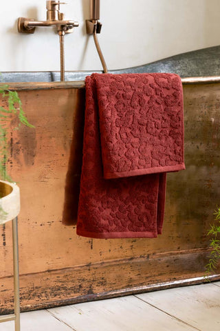 The Leopard Jacquard Towel in Burnt Brick styled against a copper bath tub. 