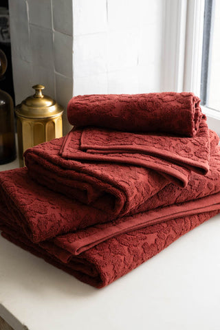 The Leopard Jacquard Towels in Burnt Brick shown folded together on the windowsill of a bathroom. 