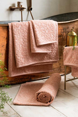 All sizes of the Leopard Jacquard Towels in Dusty Pink shown in a white bathroom, with the towels hung over a copper bath and displayed rolled on the floor. 
