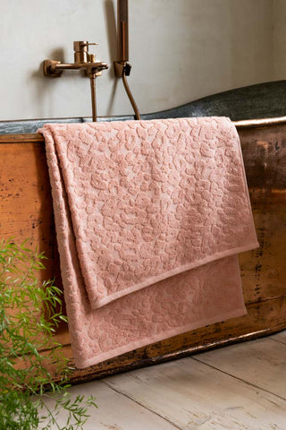A Large Leopard Jacquard Towel in Dusty Pink shown in a white bathroom against a copper bath tub. 