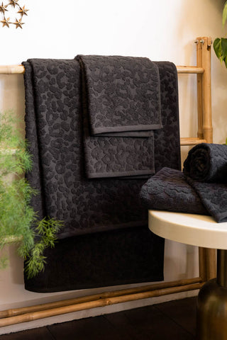 Leopard Jacquard Towels in Jet Black styled on a bamboo towel rail against white walls. 