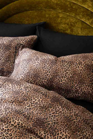 The Leopard Love Duvet Cover and Pillow Case Set styled on a bed with black pillowcases and a green velvet headboard.