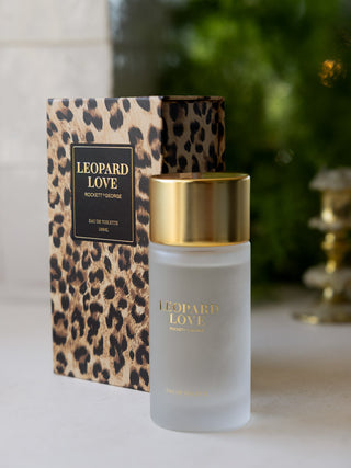 The Leopard Love Eau de Toilette - 100ml and box on a white surface with greenery in the background.