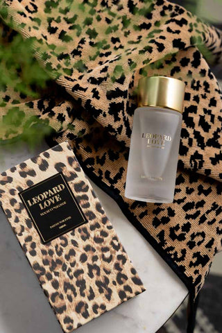 The Leopard Love Eau de Toilette - 100ml and box styled on some leopard print fabric with some greenery.