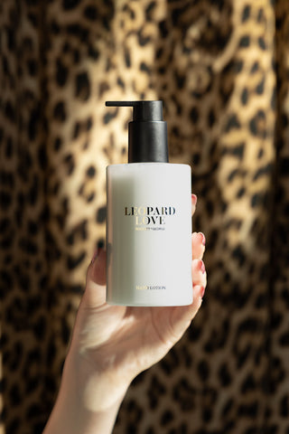A hand holding the lotion from the Leopard Love Hand Care Duo Gift Set, with a leopard print background.