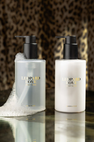 The Leopard Love Hand Care Duo Gift Set displayed on a dark surface with some bubbles on one of the bottles, with leopard print in the background.