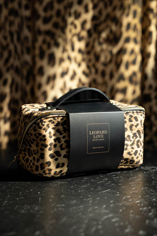 The Leopard Love Makeup Bag Beauty Gift Set in its packaging, styled on a dark leopard print surface with leopard print in the background.