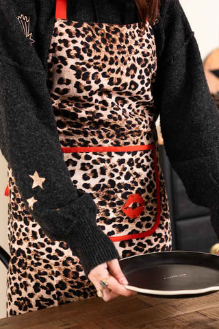 Person wearing a leopard print apron with red accents, holding a black plate.