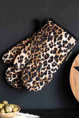 The Leopard Love Print Oven Mitts displayed hanging in front of a dark wall.