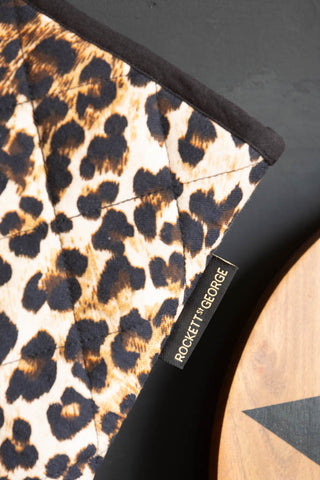 Close-up of the Rockett St George tab on the Leopard Love Print Oven Mitts, displayed in front of a black wall.