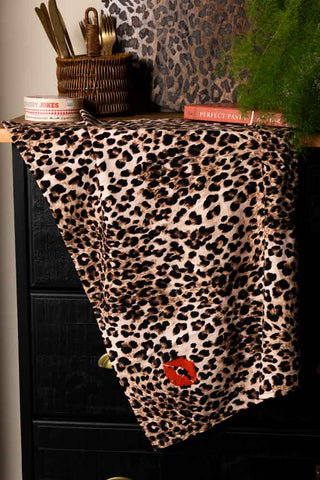 The Leopard Love Print Tea Towel hanging from a black sideboard styled with various accessories.