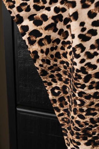 Close-up of the Leopard Love Print Tea Towel hanging in front of a black sideboard.