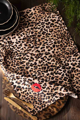 The Leopard Love Print Tea Towel displayed laid out a wooden surface with a serving boards, some plates and some cutlery.