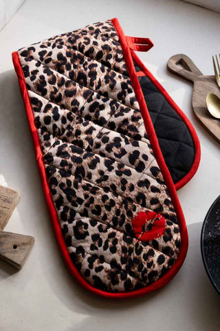 The Leopard Love Print & Red Detailing Oven Gloves displayed on a kitchen worktop with some other kitchen accessories.
