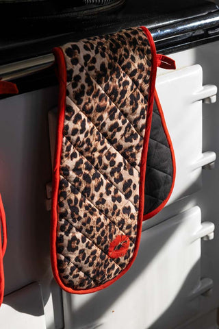 The Leopard Love Print & Red Detailing Oven Gloves displayed on the front of a range cooker.