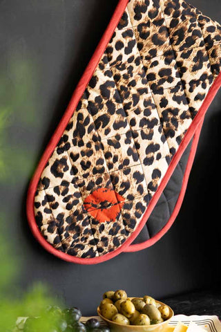 The Leopard Love Print & Red Detailing Oven Gloves hanging in front of a dark wall.