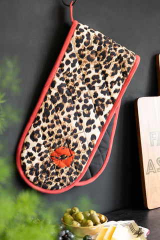 The Leopard Love Print & Red Detailing Oven Gloves displayed hanging in front of a dark wall.