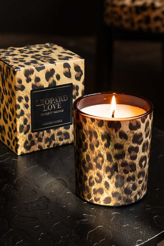 The Leopard Love Scented Candle lit and displayed with the box on a leopard print surface.