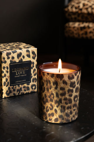 The Leopard Love Scented Candle lit, styled on a black surface with the box in the background.