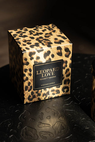 The Leopard Love Scented Candle in the box, displayed on a black leopard print surface.