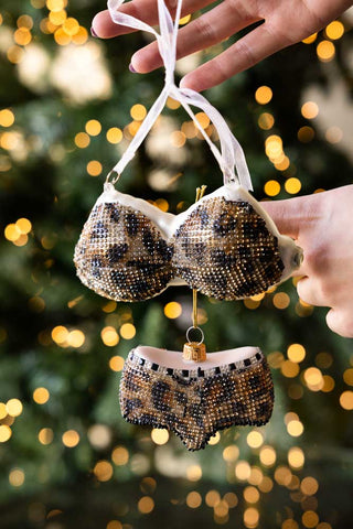 The Leopard Print Bikini Christmas Tree Decorations being held up in front of a Christmas tree with lights on.