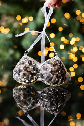 The Leopard Print Bikini Top Christmas Tree Decoration held up with lights in the background.