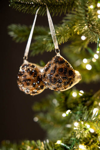 The Leopard Print Bikini Top Christmas Tree Decorations being held up in front of a Christmas tree with lights on.
