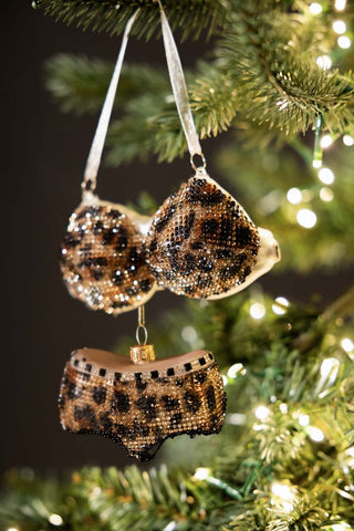 The Leopard Print Bikini Christmas Tree Decorations being held up in front of a Christmas tree with lights on.