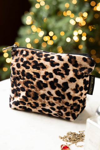 The Leopard Print Velvet Makeup Bag shown on a marble coffee table with a Christmas tree in the background. 