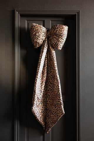 The Leopard Print Velvet Oversized Bow Decoration hanging on a black door.