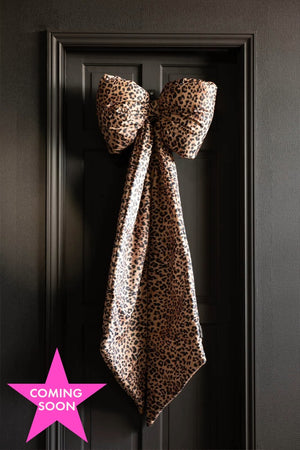 The Leopard Print Velvet Oversized Bow Decoration hanging on a black door. The image includes a pink star icon that reads 'coming soon'.