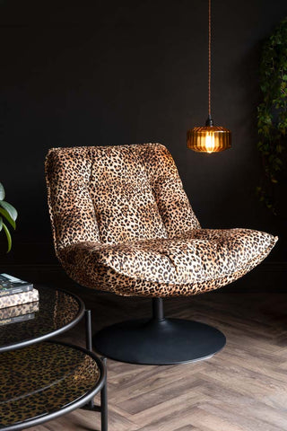 The Leopard Print Velvet Swivel Chair styled with a light next to it and various other homeware items.
