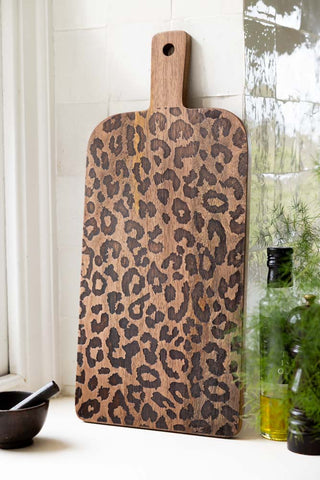 The Leopard Print Tall Wooden Serving Board shown in a kitchen against white zellige tiles. 