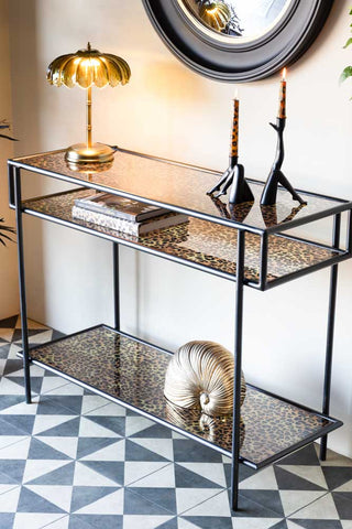 The Leopard Print & Glass Console Table displayed with various accessories on in front of a wall.