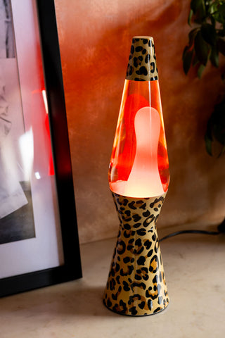 The Leopard Print & Red Lava Lamp shown on against plaster walls with a plant in the background. 