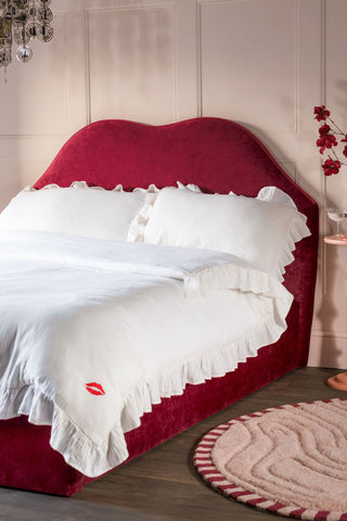 The Lips Bed in Cherry Red Needlecord Velvet  shown with white ruffled bedding. 