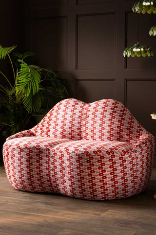 The Lips Print Velvet Lips Sofa seen from an angle, styled in front of a dark wall with a plant and cluster light.