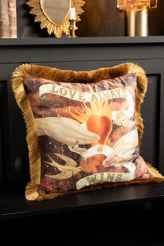 The Love Always Wins Fringed Velvet Cushion on a black bench in front of a sideboard.